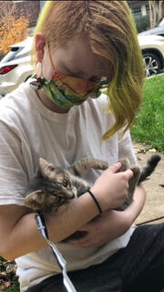 A photo of a white teenager cradling a gray tabby kitten as one would a newborn.